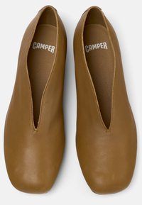 Zapatos marrones de cuero sin cordones con forma ancha en la punta, que presentan un corte en V profundo y un diseño minimalista. En el interior se muestra la marca "CAMPER".