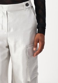 Helle silberne Cargo-Hosen mit strukturiertem Finish, seitlichem Taschen, Knopfverschluss und geradem Beinschnitt.