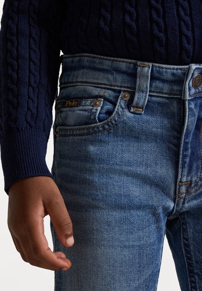Blå denimjeans med synliga sömmar, en framsida myntficka och en logotag. Matchas med en mörk stickad tröja.