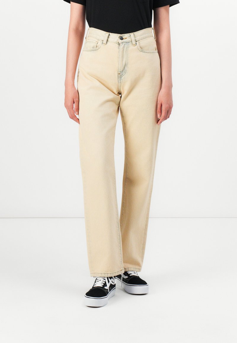 Beige high-waisted jeans with a straight-leg cut, featuring a button and zipper closure, and classic five-pocket design. Worn with black sneakers.