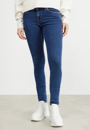 Slanke blauwe jeans van denim met een vervaagde wassing, voorzien van achterzakken, riemlussen en een rits, gecombineerd met witte sneakers.