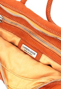 Interno di borsa arancione con esterno testurizzato, doppi cerniere argentate e fodera beige. Presenta un'etichetta del marchio "Caterina Lucchi, Made in Italy."