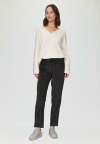 Crème gebreide trui met V-hals en lange mouwen, gecombineerd met zwarte tapse broek met een trekkoord in de taille en twee buidelzakken aan de voorkant.
