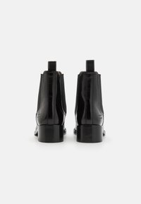 Botas de tobillo negras de cuero con textura suave, paneles laterales elásticos y tacones cuadrados. La parte trasera cuenta con lengüetas para facilitar el calzado.