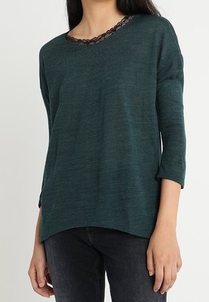 Diep teal gebreide trui met een bootnek en zwarte kanten afwerking. Heeft driekwartmouwen en een losse pasvorm met een ronde zoom.