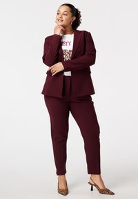 Bordeaux blazer en bijpassende broek, gelaagd over een witte graphic t-shirt met dierenprint. Gecombineerd met laarzen met luipaardprint.