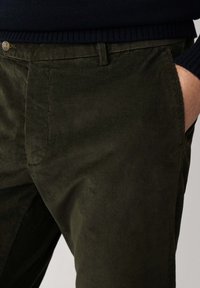 Pantaloni in velluto a coste verde oliva con texture a righe verticali, dotati di tasche laterali e chiusura con bottone. Design casual, vestibilità sartoriale.