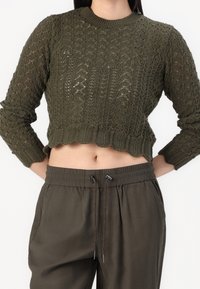 Olijfgroen, kort gebreid trui met ingewikkeld open werkpatroon en geribbelde randen, gecombineerd met bijpassende broek met trekkoord.