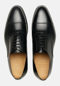 Chaussures habillées en cuir noir avec un design à lacets, texture lisse, bout arrondi et détails de couture supplémentaires sur le dessus.