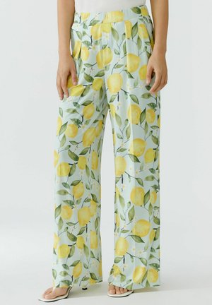 Pantalon à jambes larges avec imprimé citron jaune et feuilles vertes sur tissu bleu clair, porté avec des sandales blanches à talons et un top blanc.