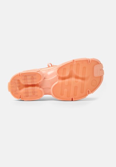 Sneaker with a textured, rubber sole in soft coral, featuring a rounded shape and grooved patterns for improved traction.