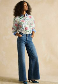 Floral-patterned white blouse with blue collar; high-waisted, wide-leg blue denim jeans; blue heels complete the look.