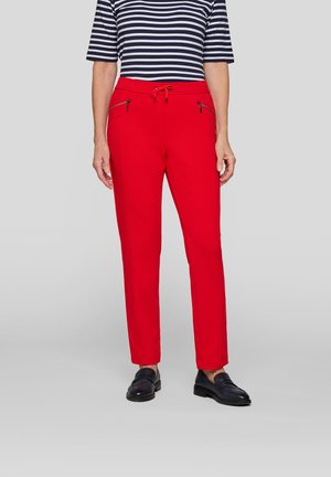 Red trousers with a drawstring waist, two front zip pockets, and a straight leg design. Paired with a navy and white striped shirt.