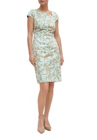 Blumenkleid mit beiger Basis und mintgrünem Design. Kurze Ärmel, taillierte Silhouette, knielang. Paar hautfarbene High Heels.