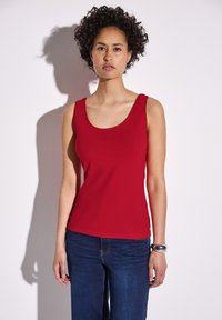 Top rosso in tessuto liscio, con scollatura a barca e design senza maniche. Abbinato a jeans blu scuro.