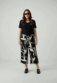 Woman wearing black sunglasses, black short-sleeve top, black and white abstract patterned wide-leg cropped pants, and black slip-on shoes.