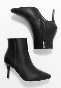 Ein Paar schwarze Lederknöchelstiefel mit spitzen Zehen, Stiletto-Absätzen und seitlichen Reißverschlüssen auf einem weißen Hintergrund.