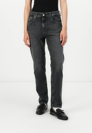 Person trägt schwarze, gewaschene Straight-Leg-Jeans mit schwarzen Lederloafers und weißen Socken, steht vor weißem Hintergrund.