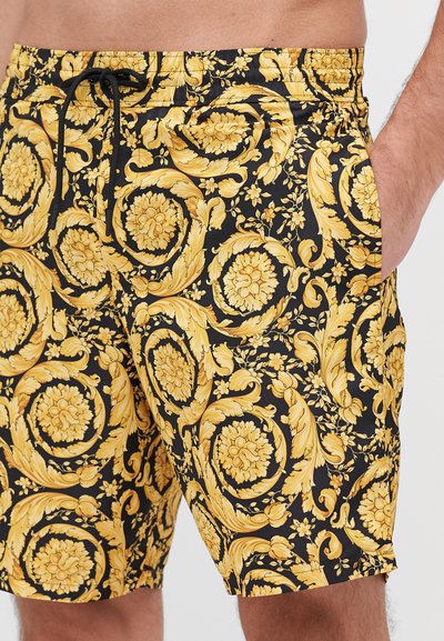 Simbyxor med svart bakgrund och intrikata gyllene blommönster. Elastisk midja med snörning och sidofickor.