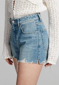 Hellblaue Jeansshorts mit fransigem Saum, hoch tailliertem Design und fünf Taschen. Das Material wirkt weich mit leichter Verblassung.