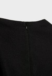 Gros plan sur l'arrière d'un vêtement noir avec une fermeture éclair dissimulée, montrant la texture du tissu et le détail du curseur de la fermeture éclair.