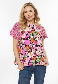 Blomsterbluse med korte, puffede ærmer, sort baggrund, livlige lyserøde, orange og grønne blomster samt blonde detaljer langs udskæringen.