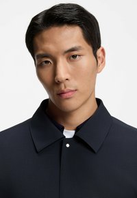 Navy blue structured shirt with a flat collar, button closure, and subtle textured fabric, designed with a clean, minimalist look.