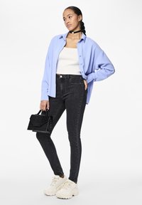 Svetlo modra prenapihnjena srajca z gumbi, bela prilegajoča majica na brezrokavnik, črne skinny jeans hlače, črna teksturirana torbica in bele masivne superge.