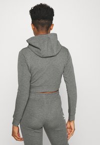 Sudadera gris corta hecha de tela suave, con una gran capucha y mangas ajustadas. Combinada con pantalones a juego, que destacan por su diseño simple.