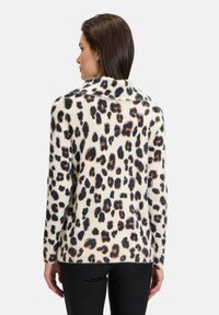 Leopardenmuster-Pullover aus weichem, fuzzy Material, mit einem cremefarbenen Grundton und schwarzen sowie braunen Flecken, langen Ärmeln und einem breiten Kragen.