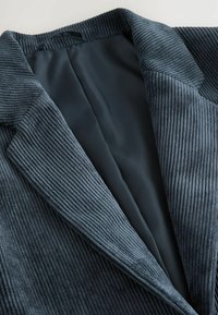 Mörkblå kordjacka med breda slag, som visar den texturerade tyget och det släta innerfodret.