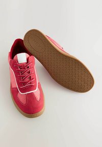 Rosafarbene Sneakers mit einem Obermaterial aus Wildleder und Stoff, weißen Akzenten, runder Zehenpartie und gemusterter Gummisohle. Die Schnürsenkel sind rot und flach.