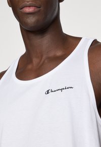 Λευκό βαμβακερό αμάνικο μπλουζάκι με κλασικό σχέδιο, στρογγυλή λαιμόκοψη και μαύρο λογότυπο "Champion" στην αριστερή πλευρά του στήθους.