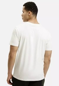 Biała bawełniana koszulka z krótkim rękawem, okrągłym dekoltem i prostym wzornictwem. Tył ma gładką teksturę i luźny krój. Styl minimalistyczny.