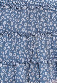 Tissu bleu avec un motif floral blanc, comportant des niveaux froncés et une finition texturée. Les détails cousus le long des bords mettent en valeur le design.