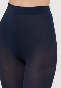 Tmavě modré legíny s hladkou texturou a širokým elastickým pasem. Mají poloprůsvitný vzhled a bezšvový design až po pas.