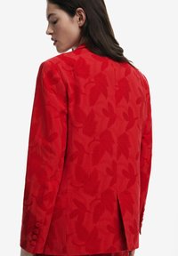 Rode blazer met een textuur motief van bladeren, getailleerde pasvorm, enkele split achter en vijf knoopdetails op de mouwen.