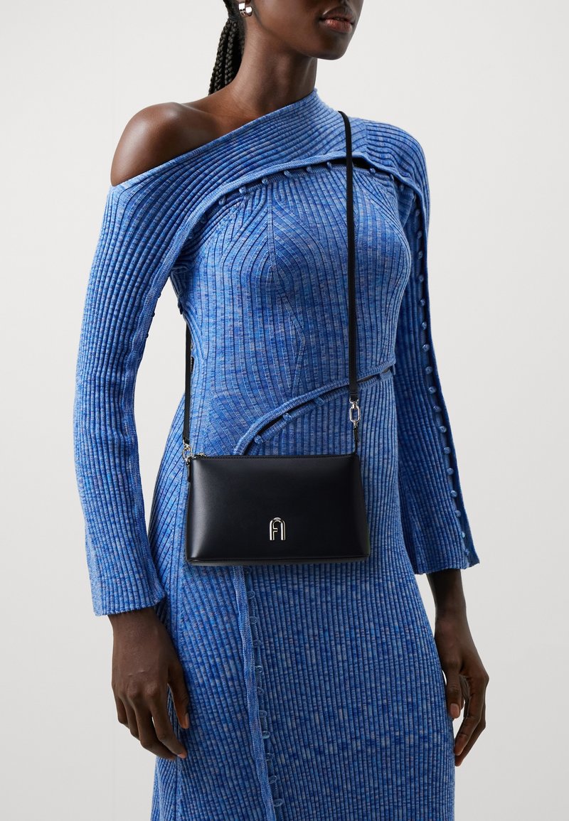 Donna che indossa un vestito aderente blu in maglia a coste con dettagli a spalle scoperte e una borsa a tracolla nera con chiusura in argento.