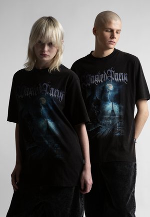 Dwie osoby w czarnych, oversize'owych koszulkach z grafiką przedstawiającą nocną panoramę miasta z błyskawicami i gotyckim pismem, stojące na tle jednolitego tła.