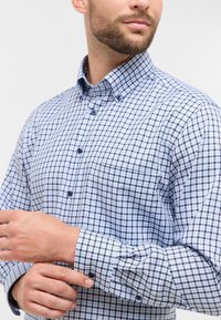 Camicia con bottoni in un motivo a quadri blu e bianchi. Presenta un colletto a punta, maniche lunghe e una tasca sul petto. Realizzata in tessuto jacquard.