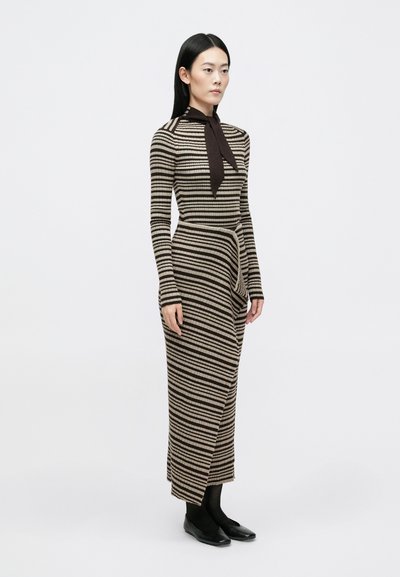 Vestuário tricotado de manga longa em listras verticais alternadas de creme e castanho. Apresenta uma silhueta ajustada com um laço na gola e drapeado lateral.