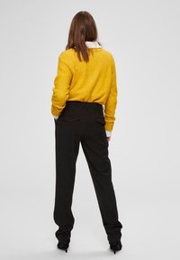 Żółty sweter o luźnym kroju i prążkowanych mankietach, zestawiony z czarnymi spodniami typu wide-leg. Sweter ma okrągły dekolt i gładką teksturę.