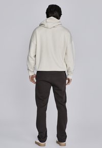 Crème hoodie met een relaxte pasvorm en capuchon, gecombineerd met donkerbruine joggingsbroek. Zachte stof en ribgebreide manchetten zijn zichtbaar. Eenvoudig design.