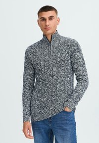 Pull en maille pour homme à col zippé en gris et bleu marine. Il présente un motif texturé, des manches longues et une coupe ajustée avec un col montant.