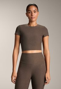 Rjav crop top s kratkimi rokavi, izdelan iz gladkega, elastičnega materiala. V kombinaciji z ujemajočimi se visokimi legicami, ki sta prav tako oprijeta.