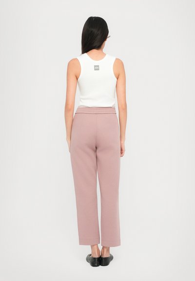 White sleeveless tank top with a back label, paired with light pink straight-leg trousers and black flats, viewed from the back.