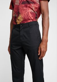 Pantaloni neri con una vestibilità su misura, caratterizzati da una texture liscia, tasche laterali e una chiusura con bottone in vita.