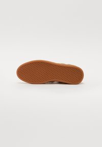 Sneaker-Sohle mit einer strukturierten GummOberfläche, die kleine kreisförmige Muster und eine braune Farbe aufweist, konzipiert für Grip und Langlebigkeit.
