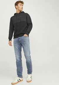Sudadera negra y gris con un logo en la parte frontal, jeans de mezclilla azul claro y zapatillas blancas con acentos verdes. Textura suave y diseño casual.