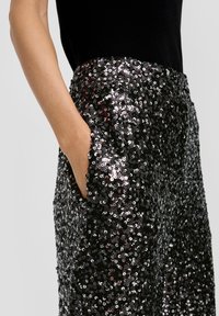 Schwarze Hose mit Paillettenverzierung und glatter Textur, ausgestattet mit einer Seitenasche und einem eng anliegenden Bund. Funkelnde, mehrfarbige Pailletten.